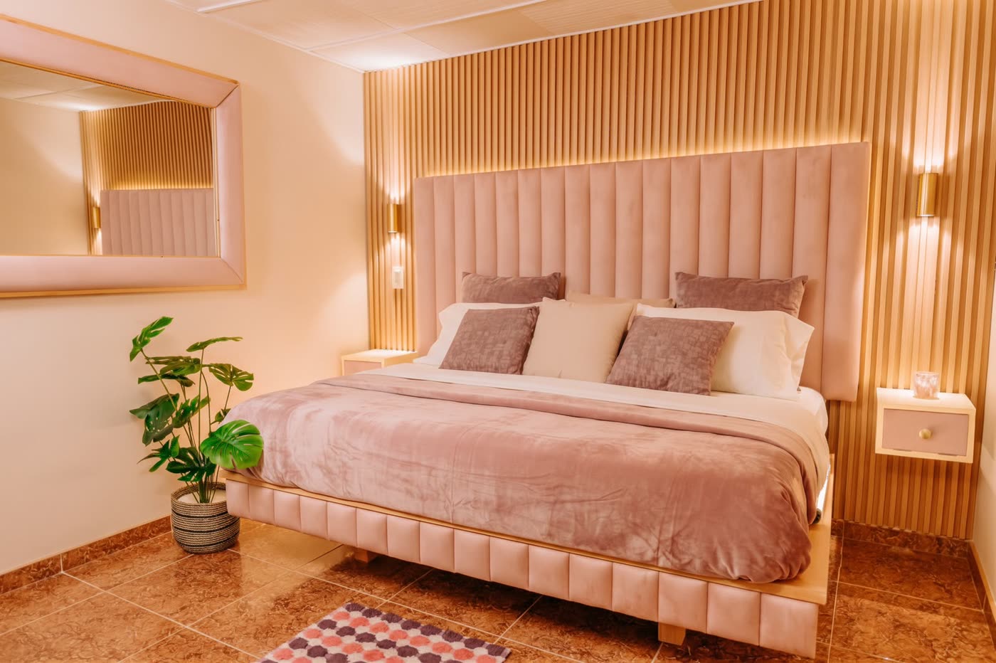 Room Rosé con cabecero de terciopelo rosado y pared de listones iluminada